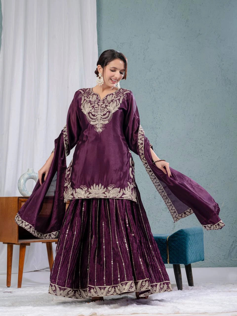 Woman wearing a purple traditional outfit with intricate designs in a minimal indoor setting.