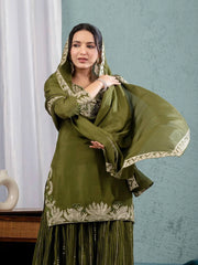 Woman wearing a green traditional outfit with a matching dupatta against a light blue wall.