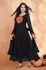 Woman wearing a black dress with orange embroidery against a beige background