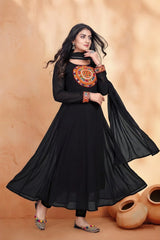 Woman wearing a black dress with orange embroidery against a beige background