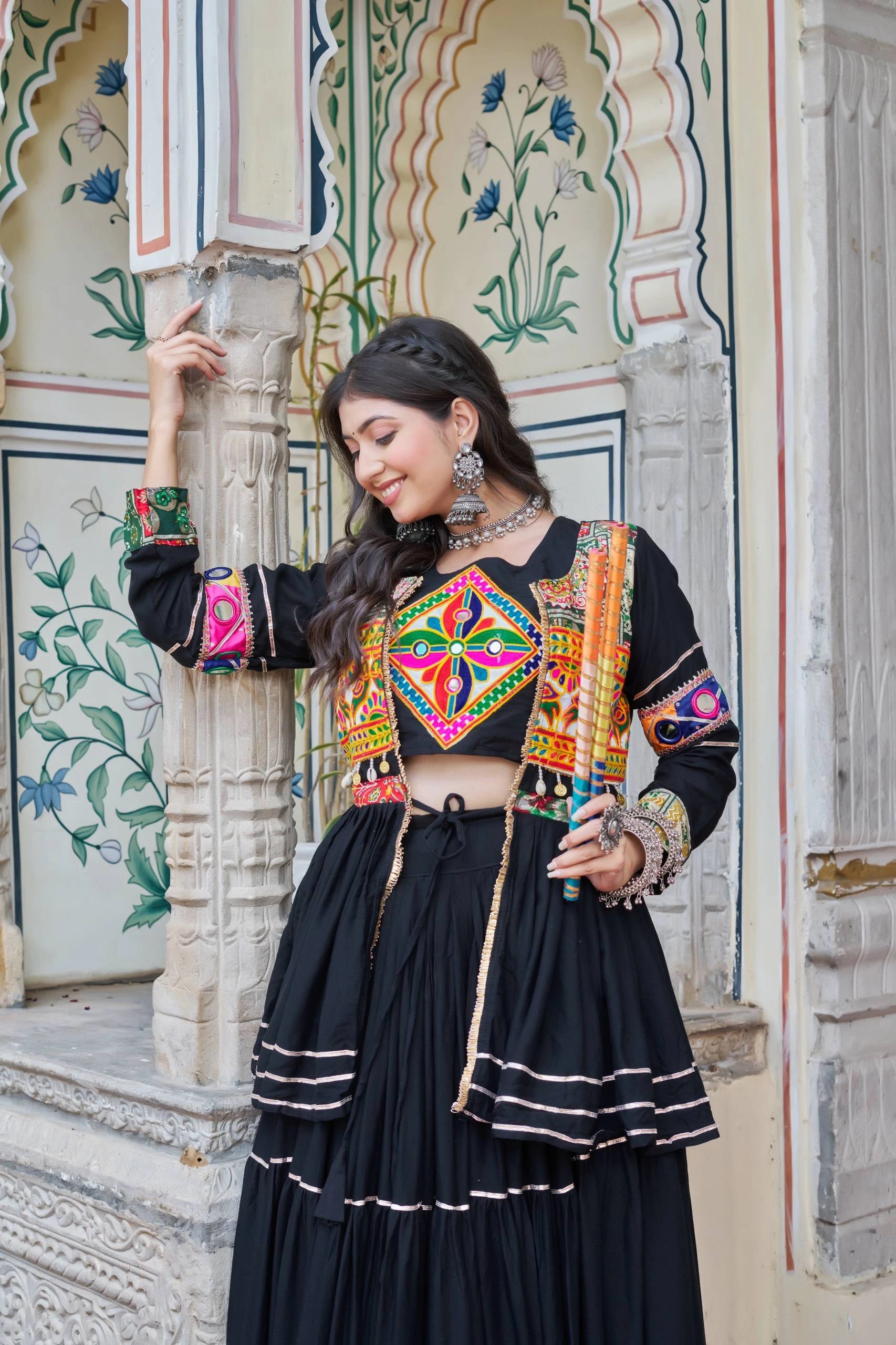 Woman in traditional outfit with colorful embroidery standing in front of an ornate wall.