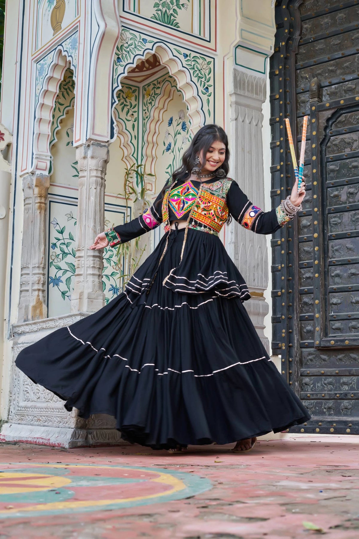 Woman in a traditional black outfit with colorful embroidery standing in front of an ornate building.