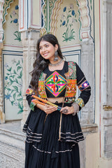 Woman in traditional outfit with colorful patterns standing in front of an ornate architectural background.