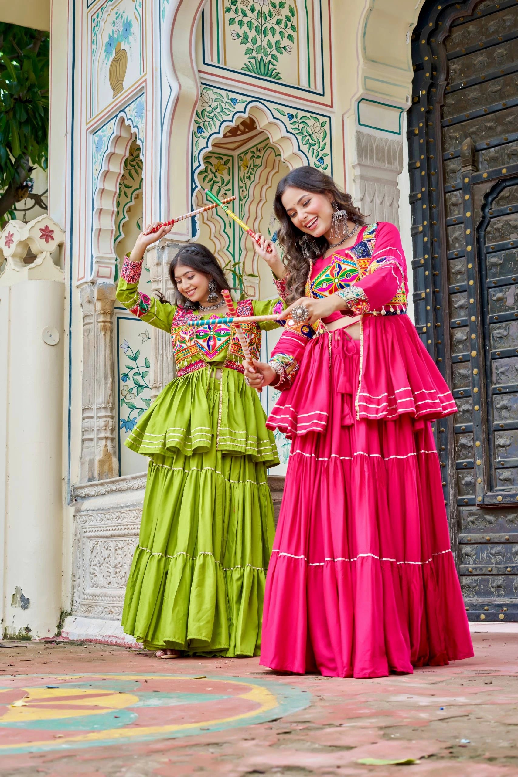 Two women in colorful traditional dresses standing in front of an ornate building.