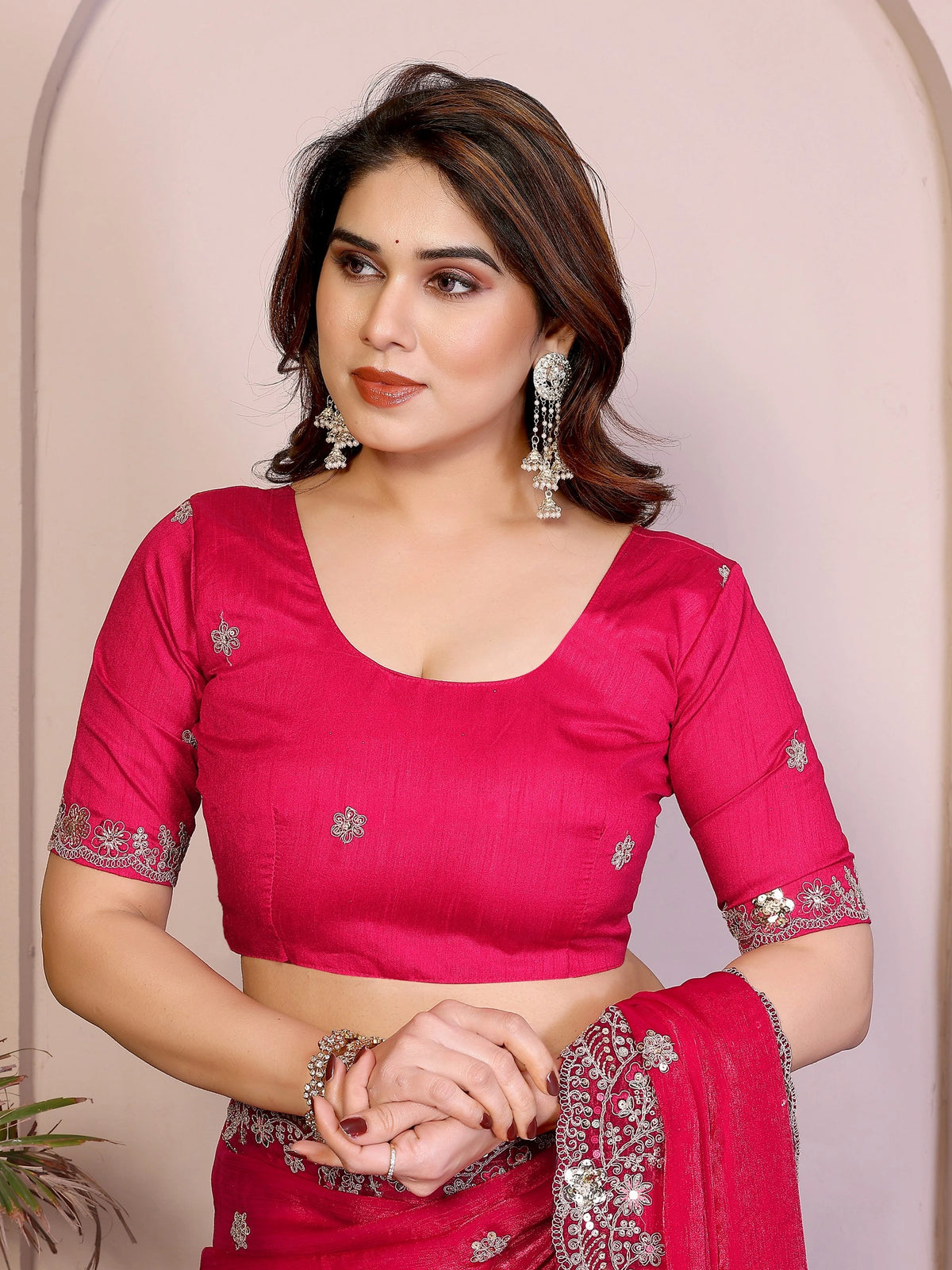 Woman wearing a pink saree with silver embroidery against a beige background