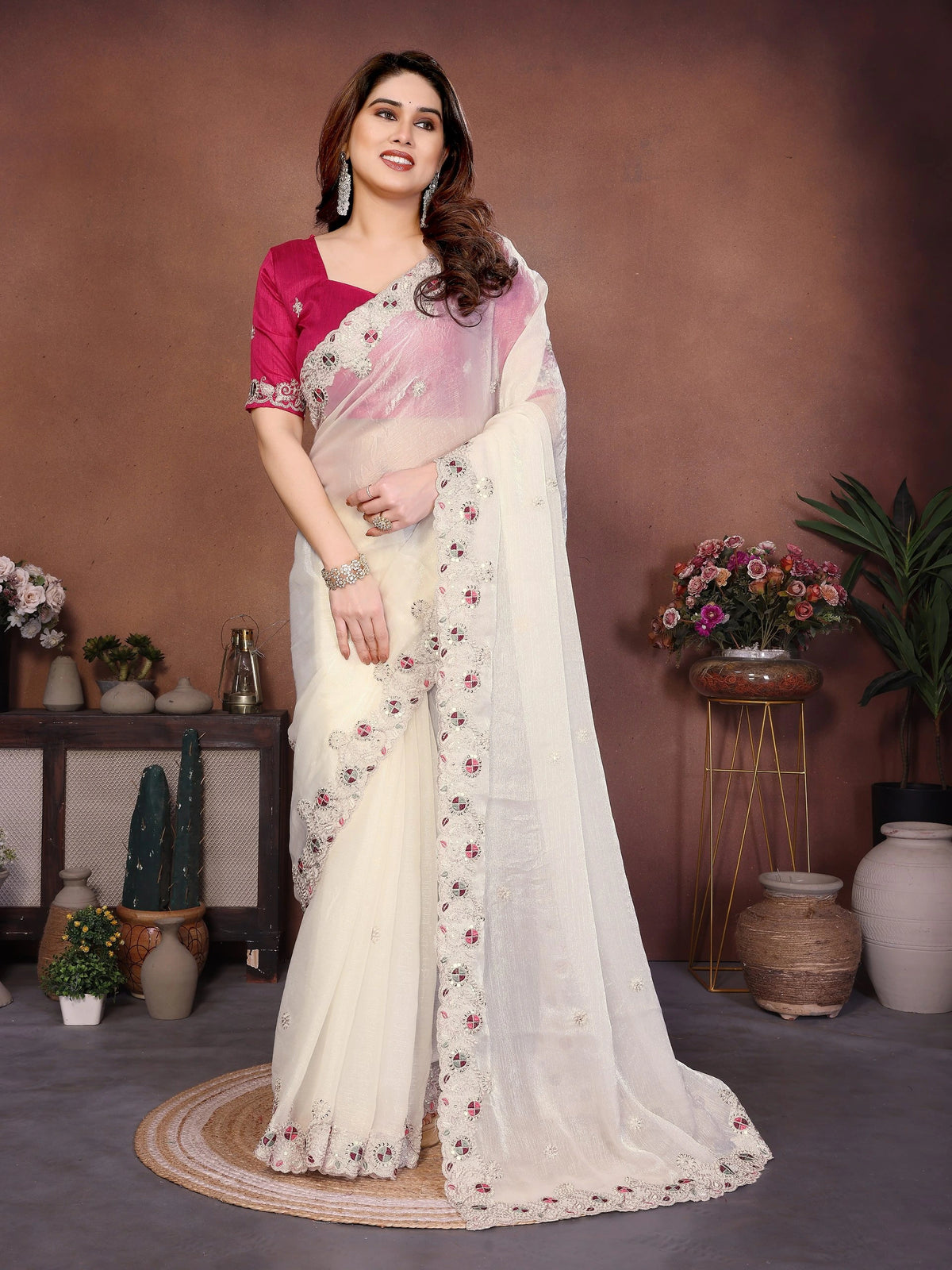 Woman wearing a white saree with pink blouse in a decorated room.