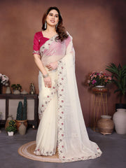 Woman wearing a white saree with pink blouse in a decorated room.