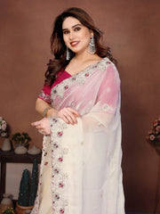 Woman wearing a white saree with pink blouse against a brown background