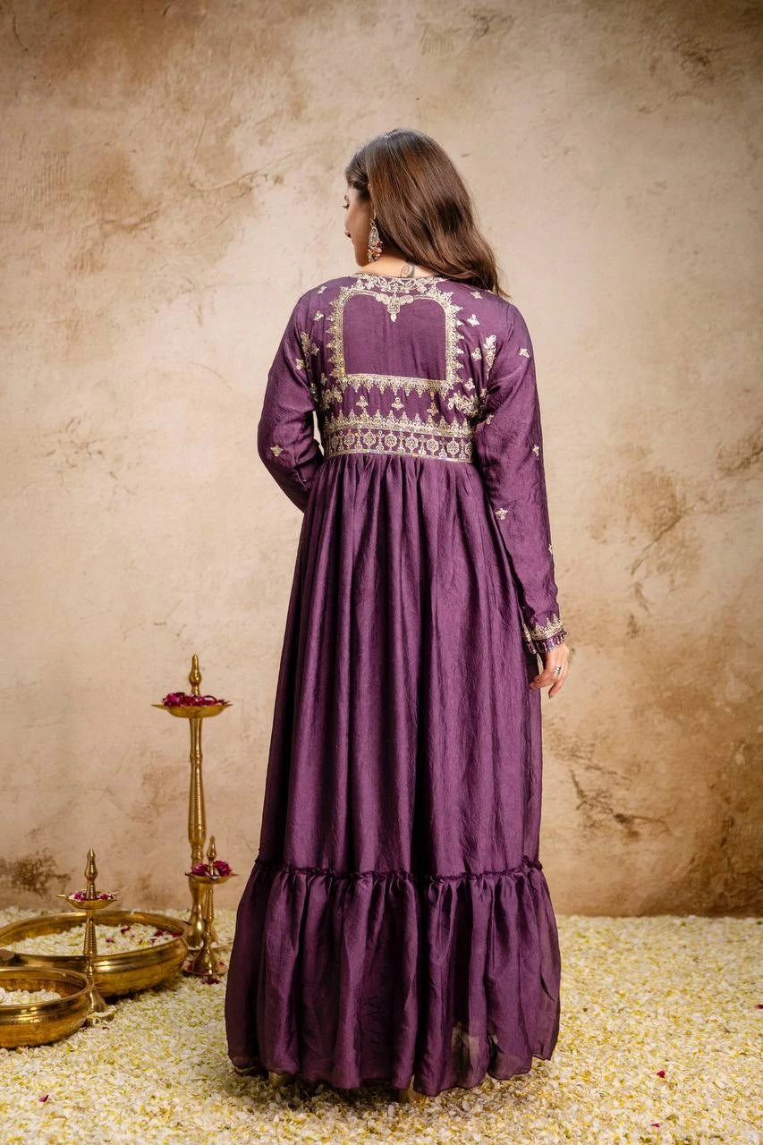 Woman wearing a purple embroidered dress against a textured beige wall.