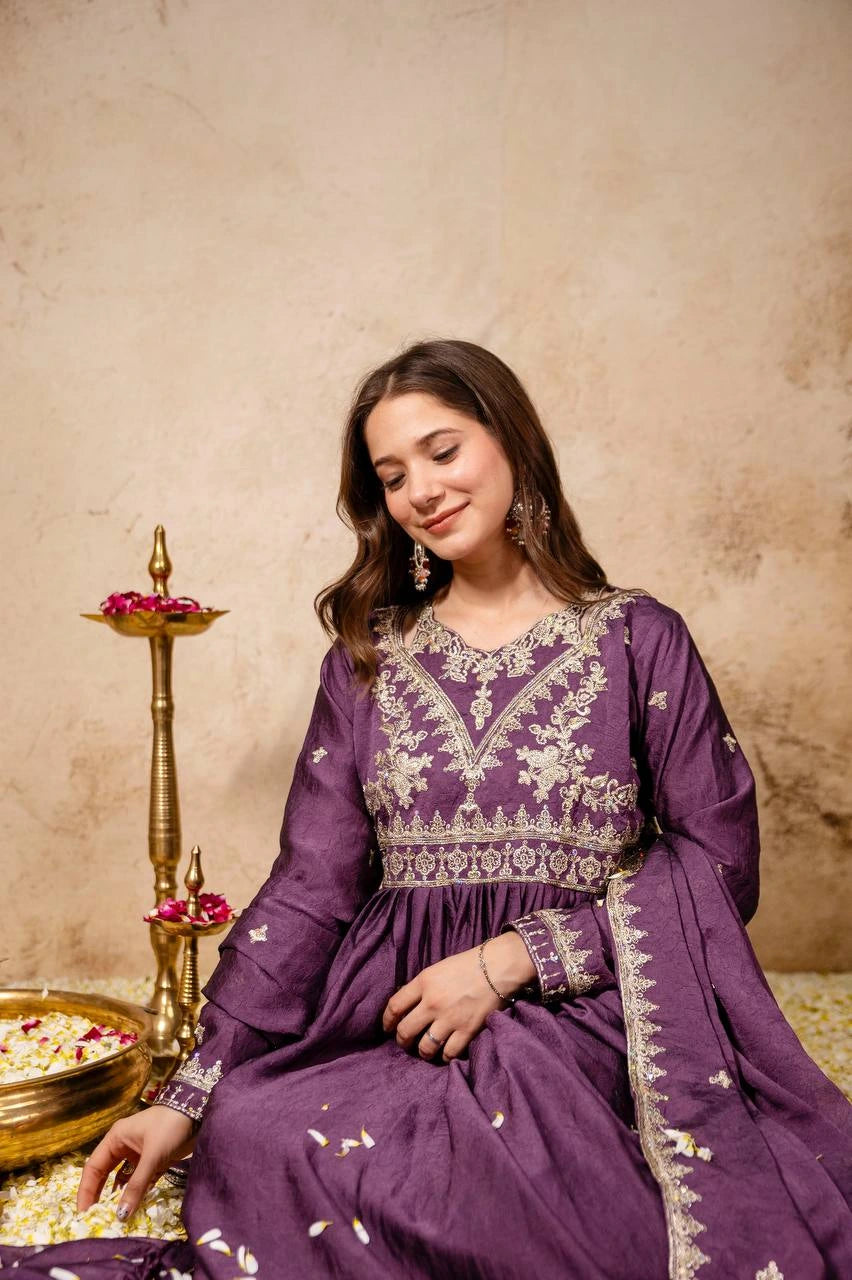 Woman in a purple embroidered outfit sitting on a textured floor with decorative items.