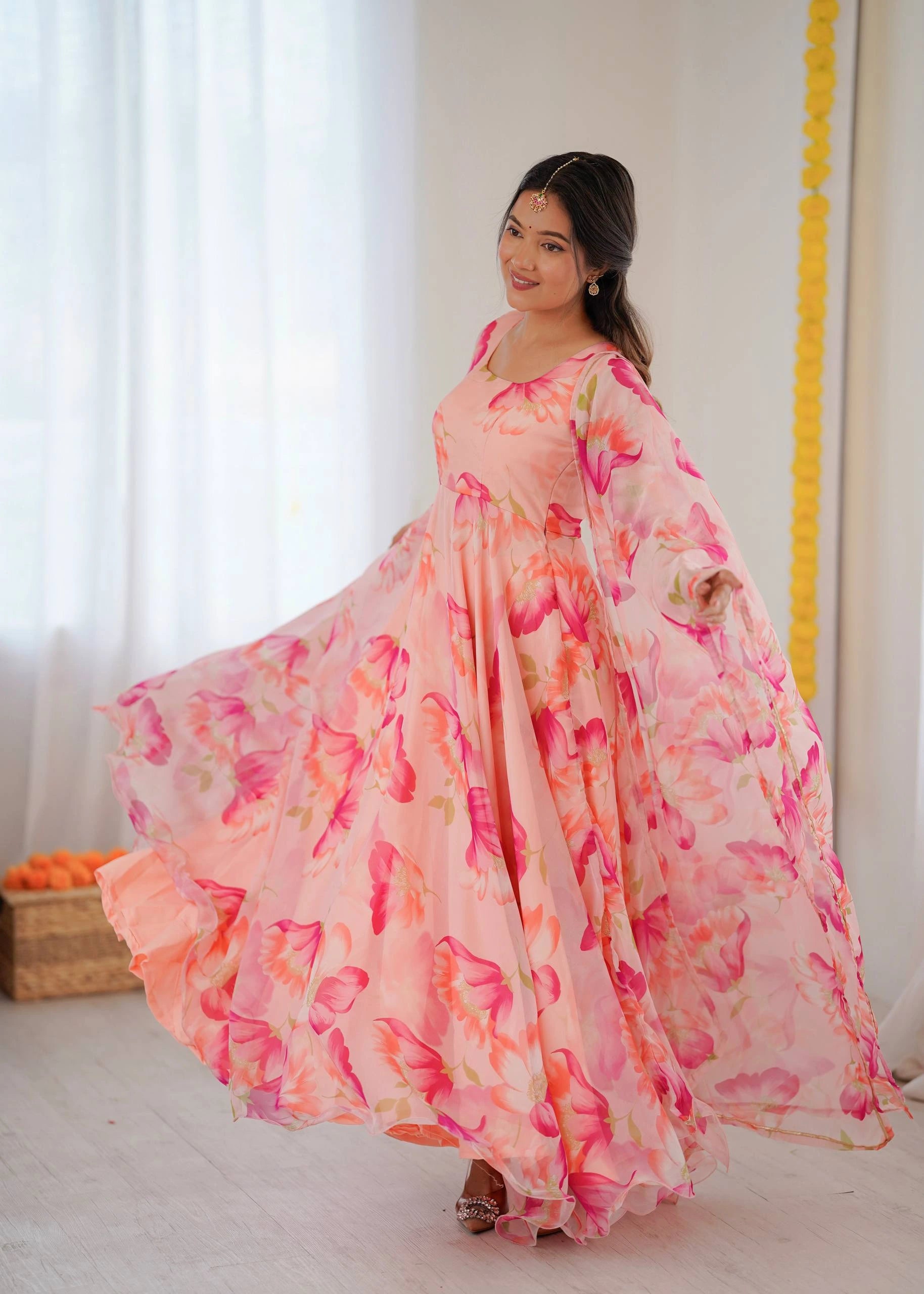 Woman wearing a long, floral-patterned dress in a bright room.