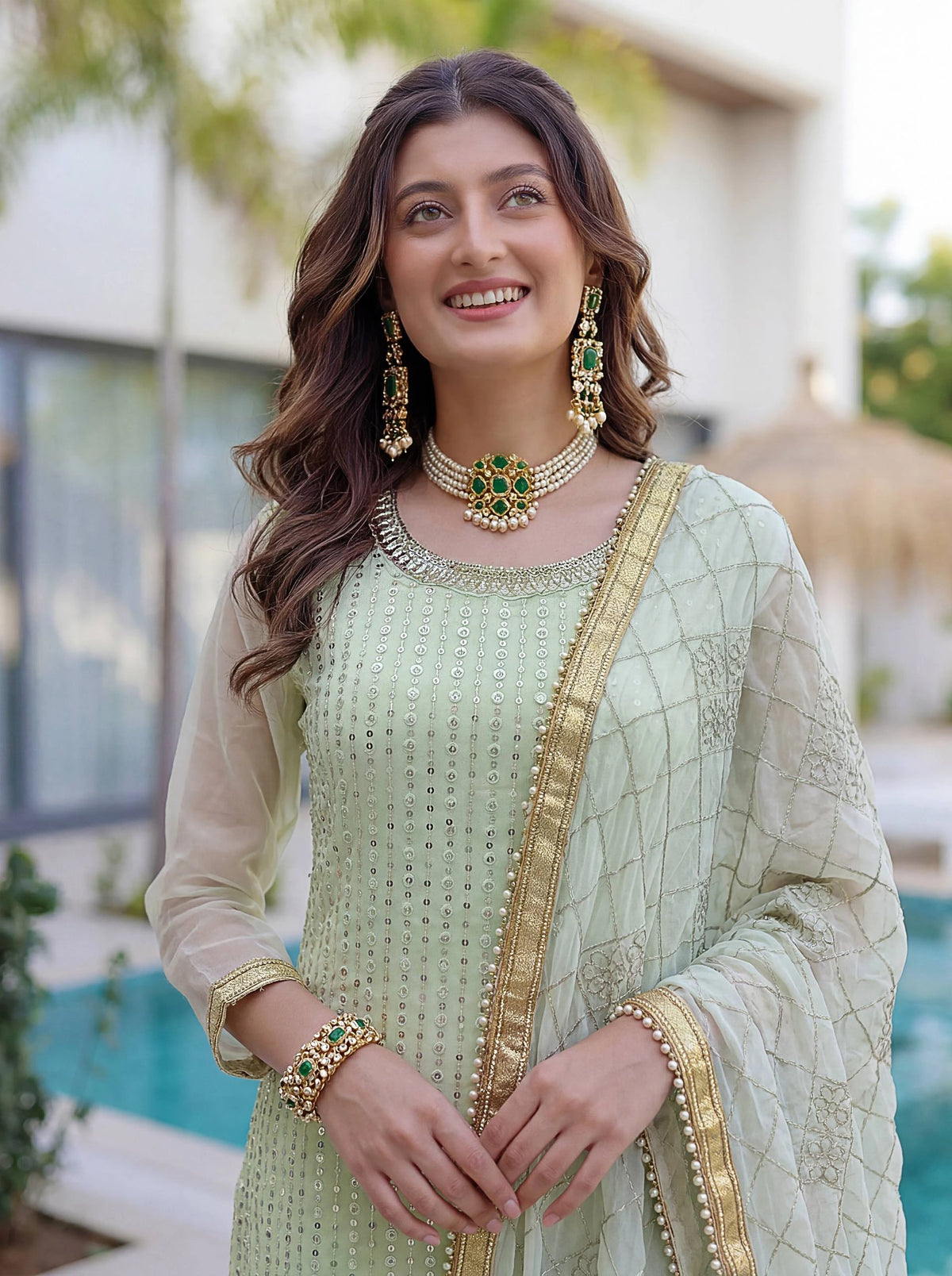 Woman in traditional attire with jewelry, standing outdoors.