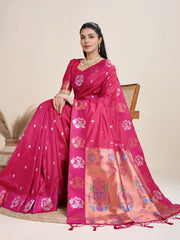 A woman models a luxurious Deep Fuchsia Soft Silk Saree. The saree features silver Zari motifs on the body and a wide pallu in contrasting rose gold, richly woven with multi-colored peacock and floral designs. She wears a matching short-sleeve pink blouse and heavy gold Kundan jewelry, posing indoors.