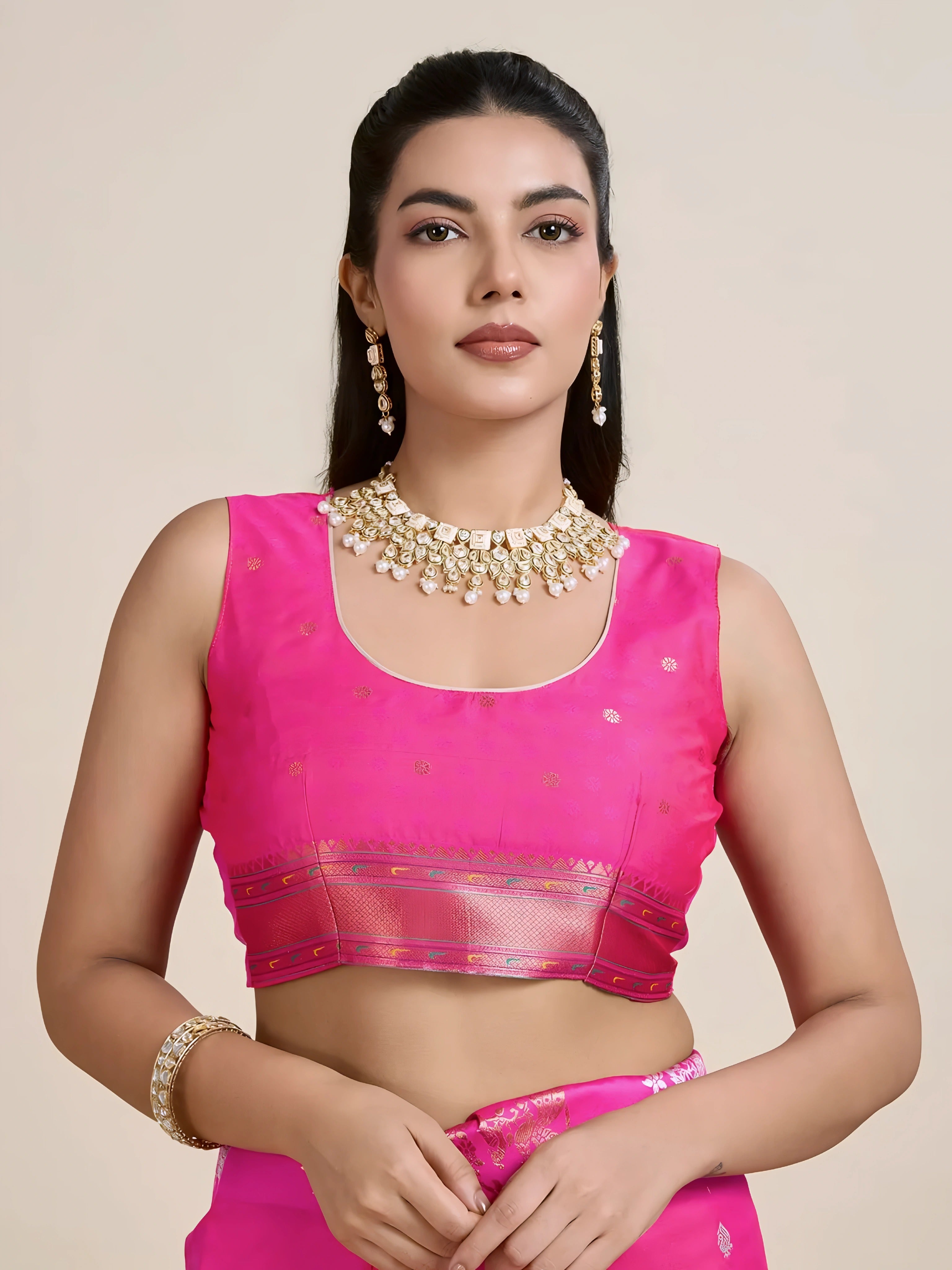 A woman models a luxurious Rani Pink Soft Silk Saree. The saree features scattered metallic motifs and a wide pallu in contrasting copper/rose gold, richly woven with multi-colored peacock and floral designs. She wears a matching pink sleeveless blouse and heavy gold Kundan jewelry, posing indoors.