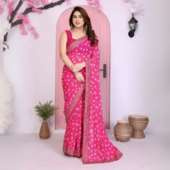 Woman wearing a vibrant pink bandhani saree with traditional white tie-dye patterns and a decorative embroidered border, paired with a sleeveless matching blouse. She stands gracefully in front of a pastel pink arched doorway, accessorized with statement earrings and bangles, surrounded by earthy clay pots, a small green foliage vase, and pink decorative branches in a contemporary minimalist studio setting.