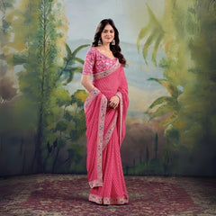 Woman wearing pink saree with floral embroidered border and matching blouse in studio backdrop