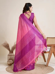 A woman models a striking Hot Pink Raw Silk Saree. The saree has a wide, vibrant purple border featuring traditional temple weaving. The pallu has wide horizontal stripes in purple. She wears a sleeveless purple blouse and a heavy gold choker necklace.