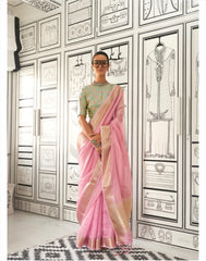 Woman in a pink zari work saree standing indoors against a backdrop of black-and-white fashion illustrations on the walls