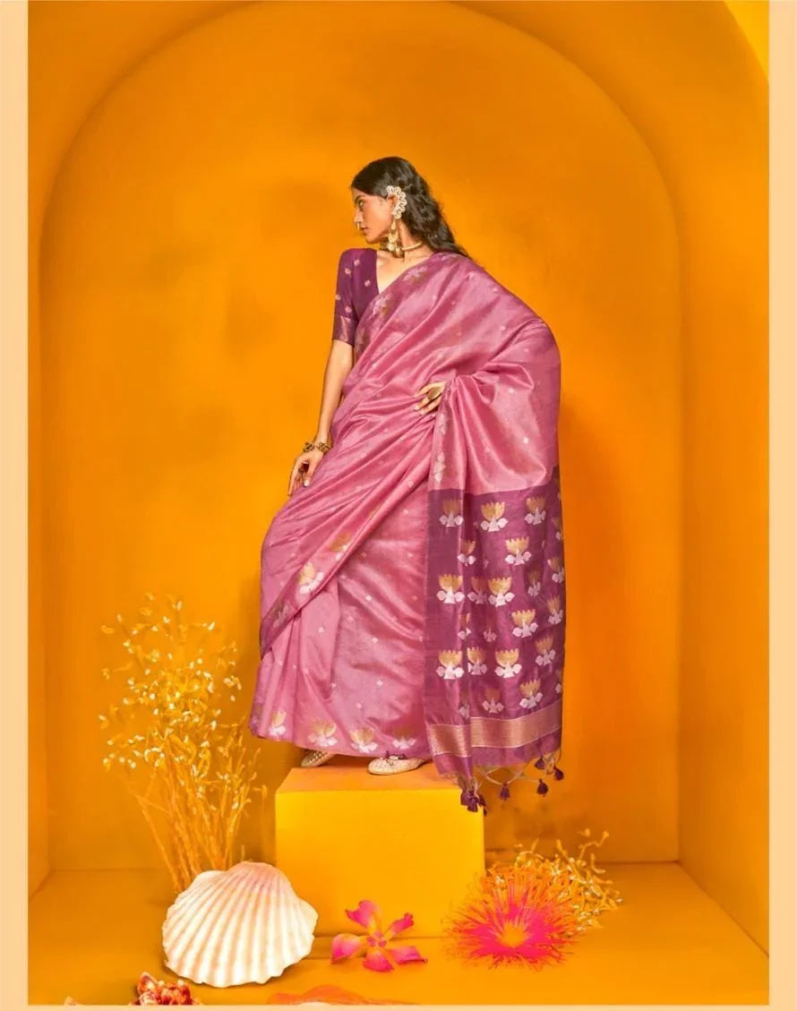Woman dressed in pink zari work saree with floral motifs and tassel border, styled with traditional jewellery, posing in a vibrant yellow arched backdrop