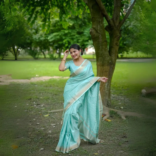 Woman in a powder blue saree with zari work posing in a park near a tree