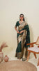 A woman models a luxurious Dark Green Soft Kanjivaram Silk Saree. The saree features striking large floral and scattered motifs woven in metallic antique gold Zari on the body and wide pallu. She wears a matching long-sleeve green blouse and accessorizes with a heavy gold Kundan choker necklace and earrings.