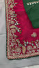 A woman models a vibrant Dark Pink Chiffon Silk Saree with scattered embellishments. The saree has a wide, intricate silver embroidery border. She wears a heavily embroidered dark green blouse and accessorizes with silver jewelry, posing indoors.