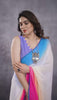 A woman models a vibrant Multicolour Georgette Silk Saree featuring a horizontal ombre color transition from blue at the top to white, pink, and peach at the bottom. The saree has a thin blue border. She pairs it with a light blue sleeveless blouse and a chunky blue and silver necklace.