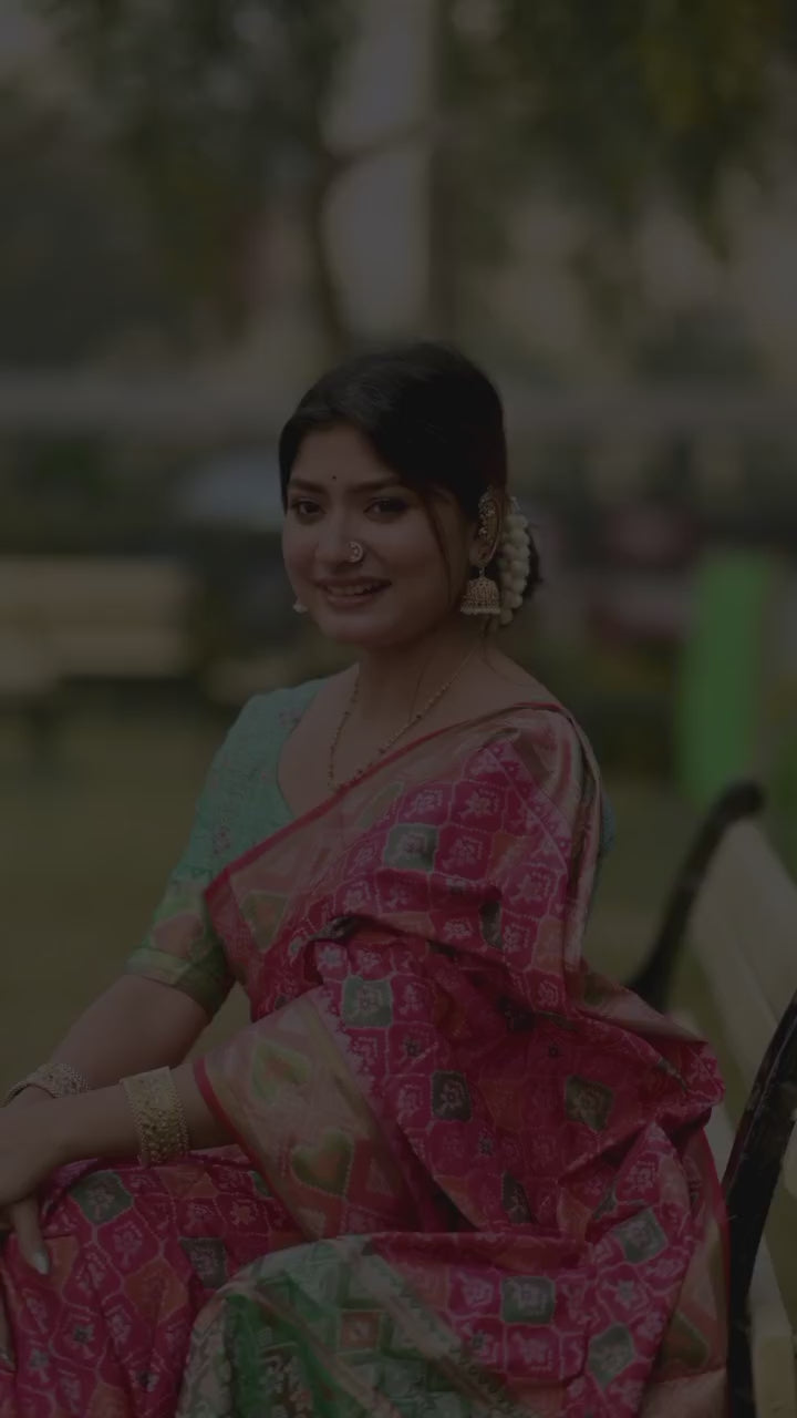 Woman wearing a red blouse and a saree with pink and green floral zari work. 