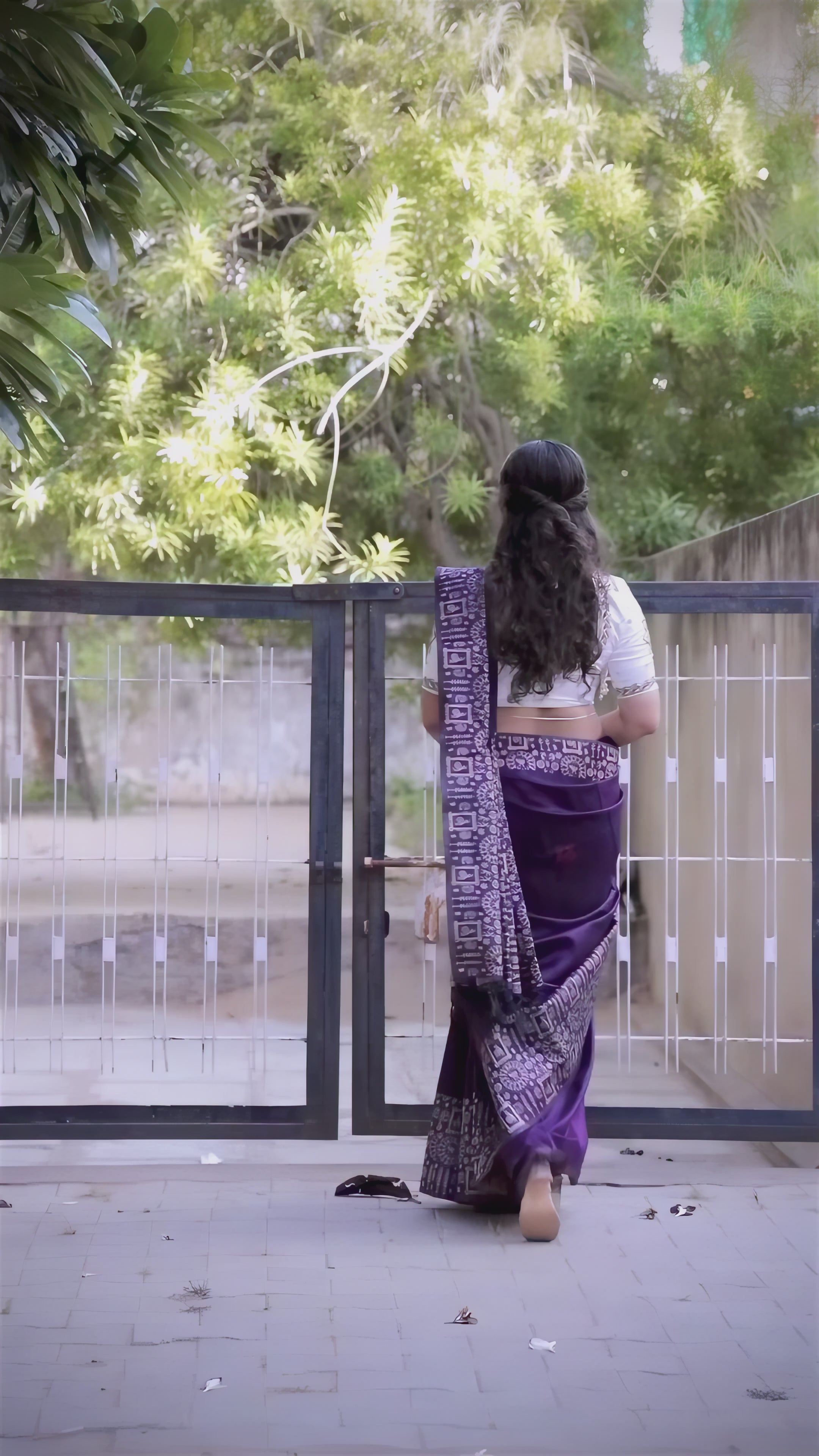 A woman models a striking Royal Purple Banglori Raw Silk Saree. The pallu and border feature dense, traditional Kalamkari-style weaving in metallic Zari thread. She wears a purple blouse and heavy green beaded jewelry, posing in an ornate, traditional setting.
