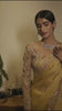 A woman models a striking Golden Yellow Soft Organza Silk Saree. The saree features delicate thread and sequin floral embroidery along the border. She wears a matching long-sleeve, heavily embroidered blouse and accessorizes with silver/diamond jewelry.