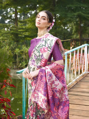 A woman models an elegant Beige Soft Tussar Silk Saree with a dense all-over print of purple, pink, and green floral and vine motifs. The pallu features a wide, contrasting deep purple panel with traditional weaving/print. She wears a matching short-sleeve purple blouse and a gold Kundan choker necklace, posing outdoors on a wooden footbridge.
