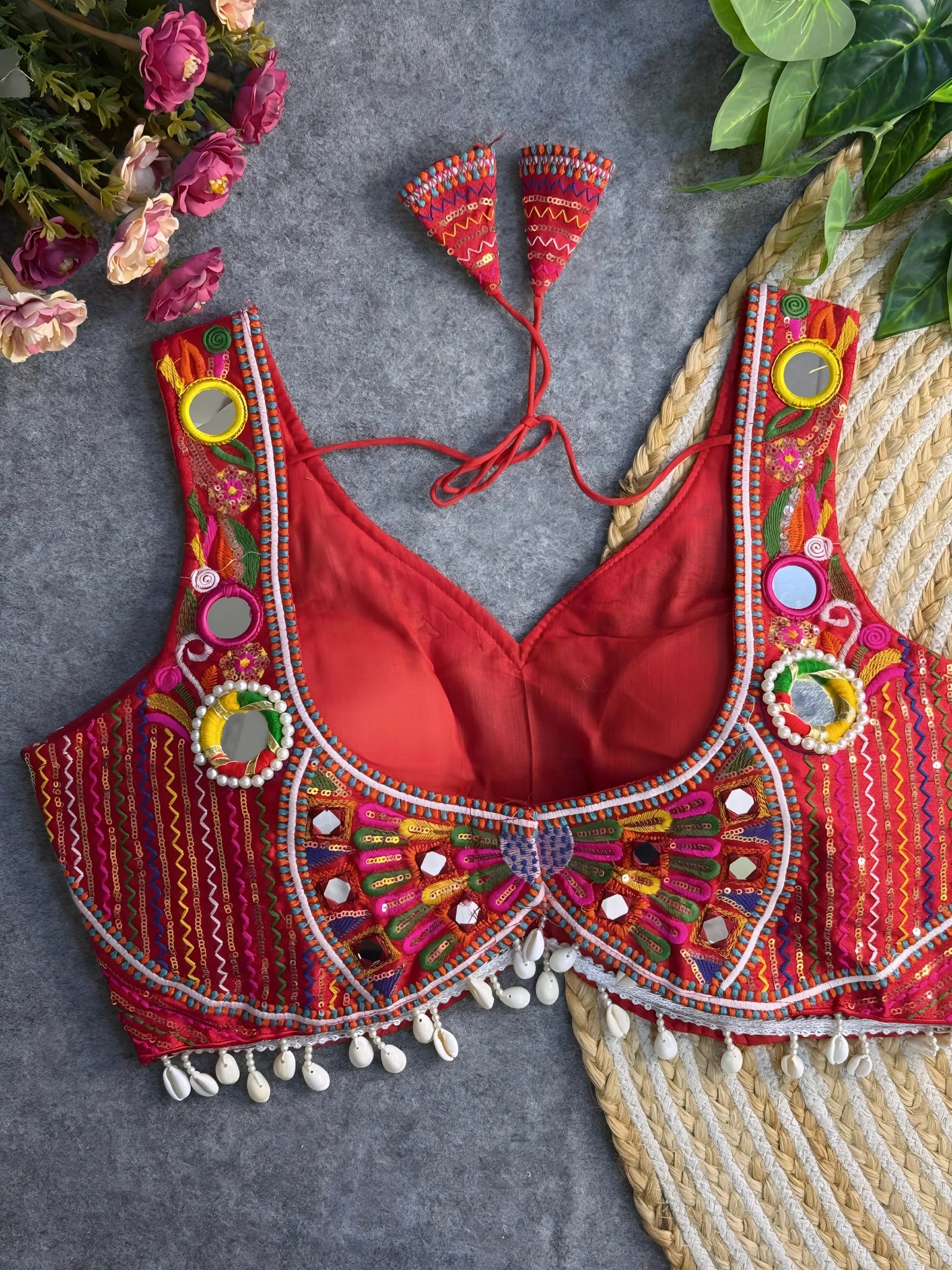 Traditional red blouse featuring vibrant multicolor mirror work, intricate thread embroidery in geometric and floral patterns, and shell tassel detailing along the hem, displayed on a flat surface with floral and leafy decor.

Related
red-multicolor-mirror-work-embroidery-blouse-shell-tassels
Traditional red blouse with vibrant mirror work, detailed embroidery, and shell tassel accents.