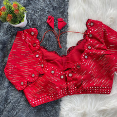 Red bridal blouse with scallop sleeves, featuring silver sequin stripes and prominent round mirror work along the neckline, sleeves, and hem, displayed on a textured grey and white fur background with a small potted plant nearby.