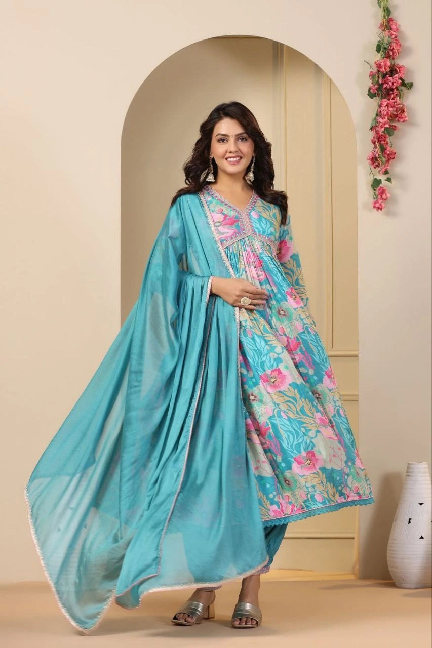 Woman wearing a floral dress with a turquoise dupatta in a decorated room.