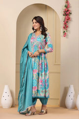 Woman in a floral dress with a blue dupatta standing in a decorated room.