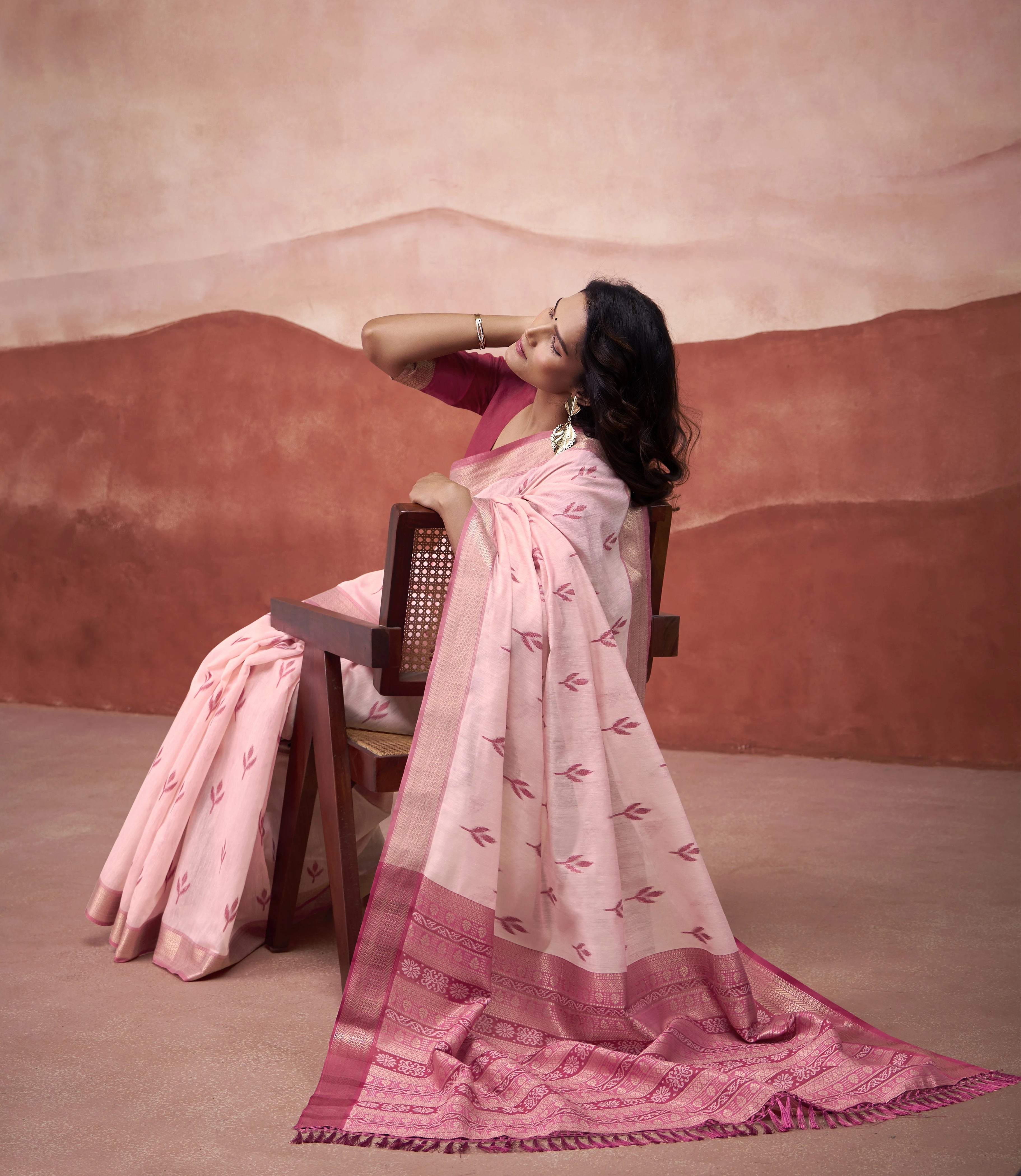 Woman in a pink saree sitting on a chair against a desert-like background