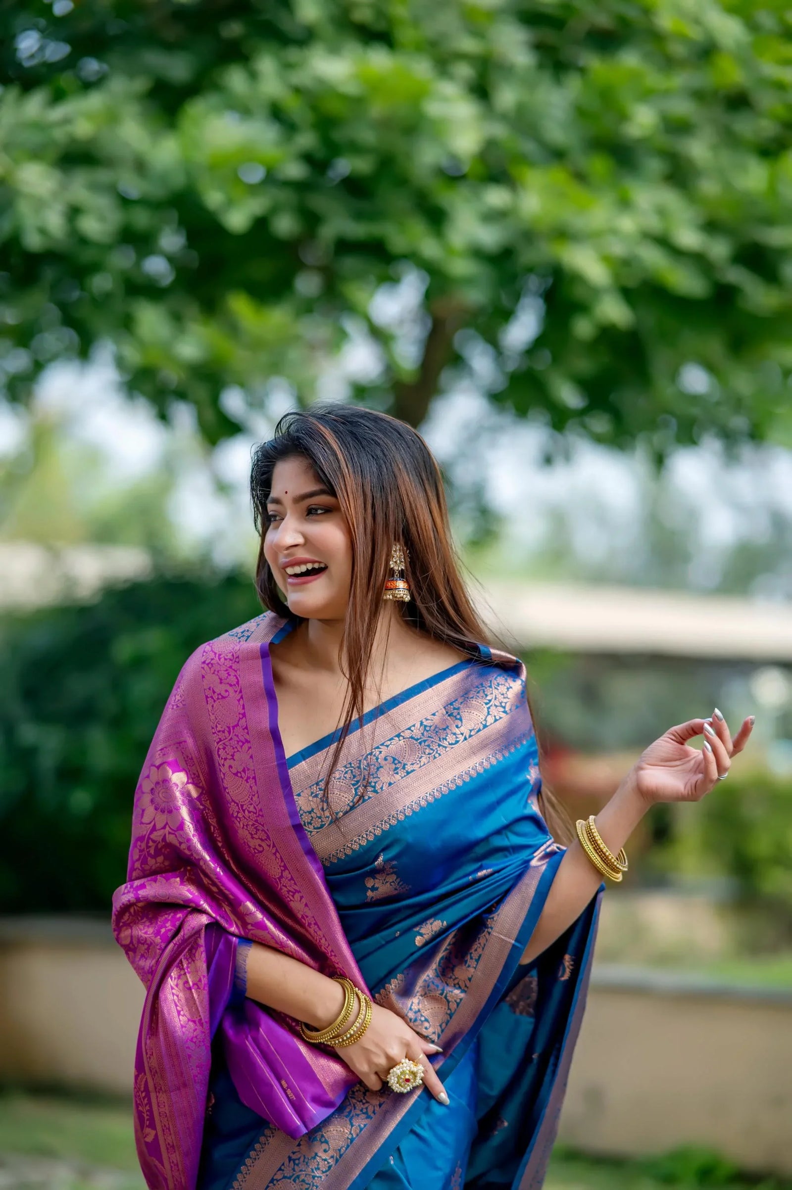 Smiling woman wearing teal blue zari work saree and traditional jewelry posing gracefully outdoors
