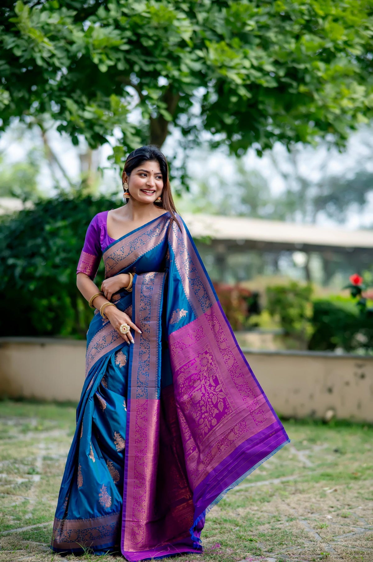 Smiling woman in teal blue zari work saree showcasing traditional Indian fashion in an outdoor setting