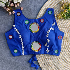 Royal-blue Indian blouse decorated with circular mirrors and cowrie shell designs, displayed flat on grey fabric and jute rug.