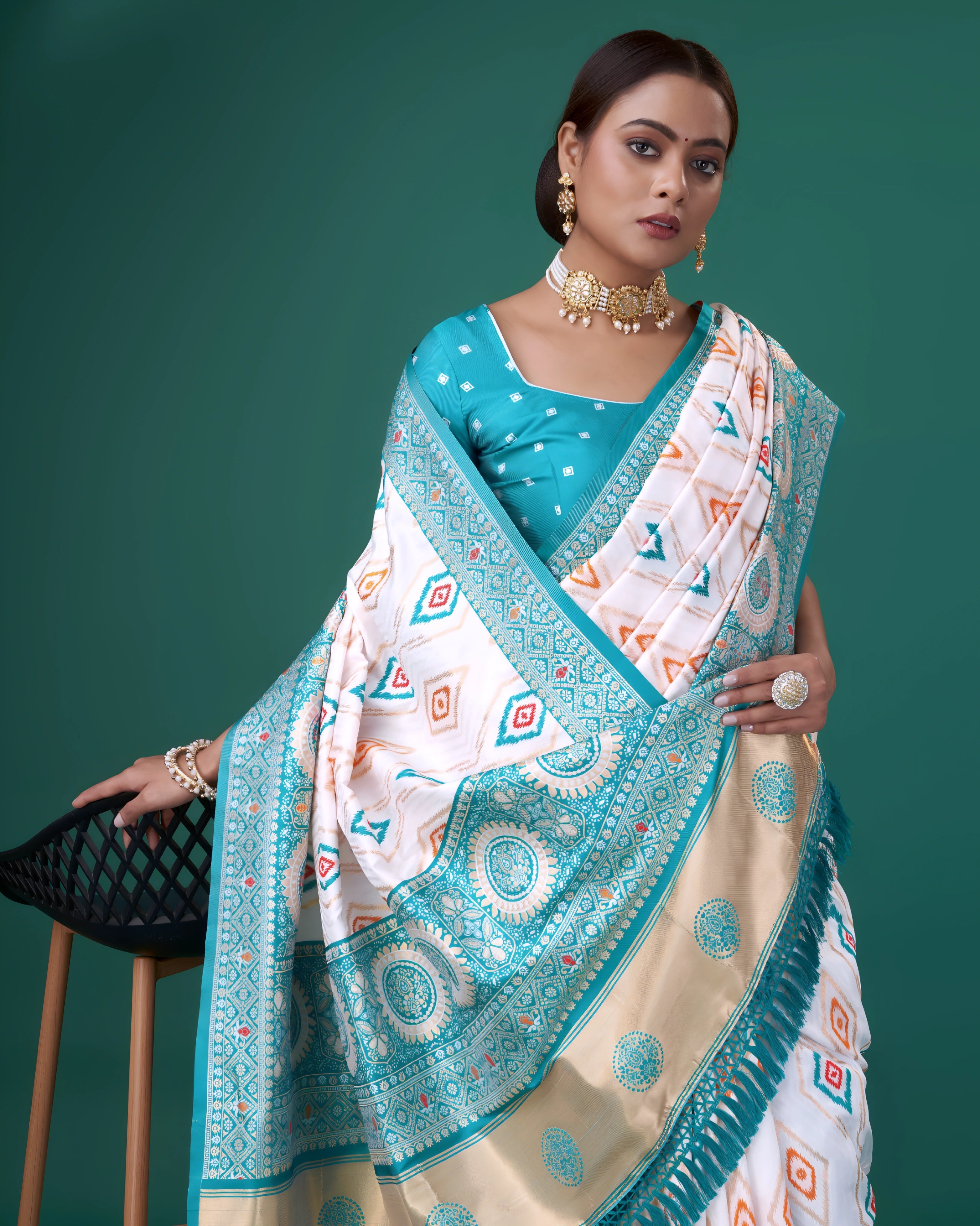 A woman models a striking White Patola Silk Saree featuring Ikat-style diamond motifs. The wide border and pallu are heavily woven in peacock blue Zari with intricate geometric patterns. She wears a blue blouse and heavy gold and pearl jewelry.