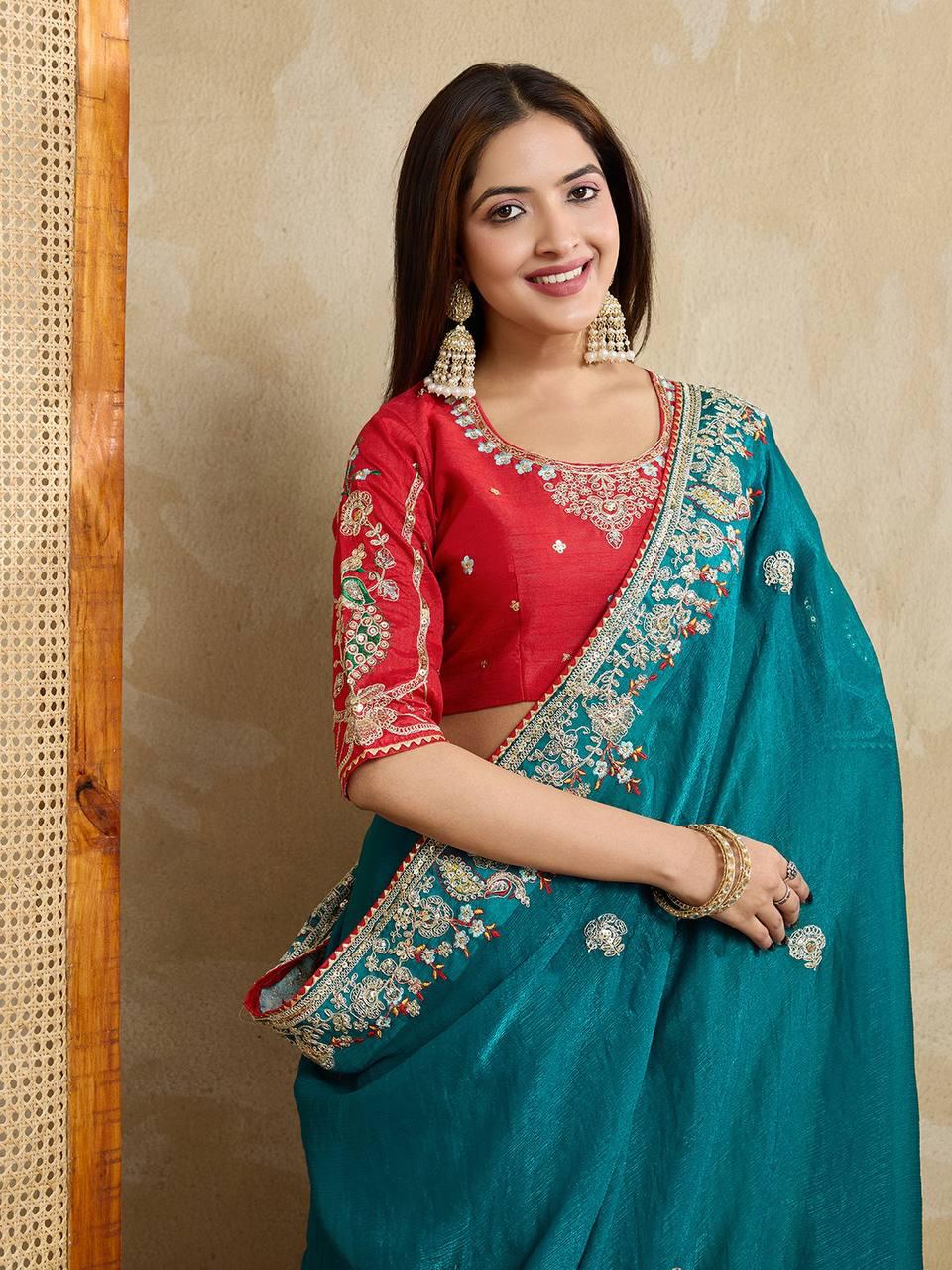 A woman models a vibrant Dark Pink Chiffon Silk Saree with scattered embellishments. The saree has a wide, intricate silver embroidery border. She wears a heavily embroidered dark green blouse and accessorizes with silver jewelry, posing indoors.