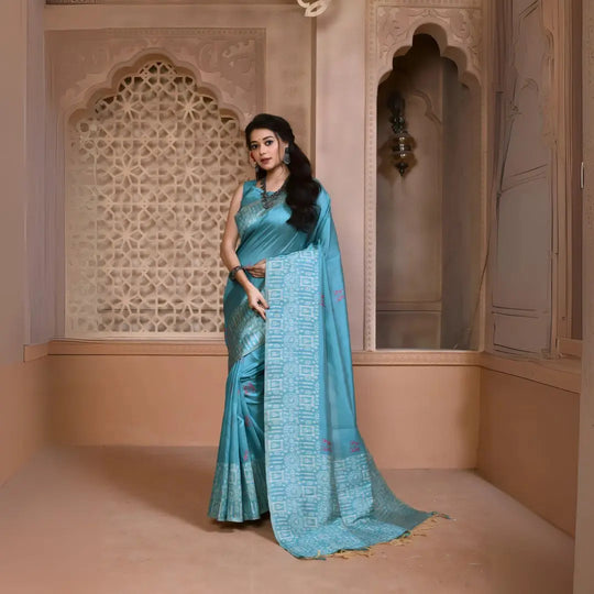 A woman models a striking Sky Blue Banglori Raw Silk Saree. The pallu and border feature dense, traditional Kalamkari-style weaving in a lighter blue metallic thread. She wears a sleeveless blue blouse and heavy oxidized silver or dark gemstone jewelry, posing in an ornate, traditional setting.