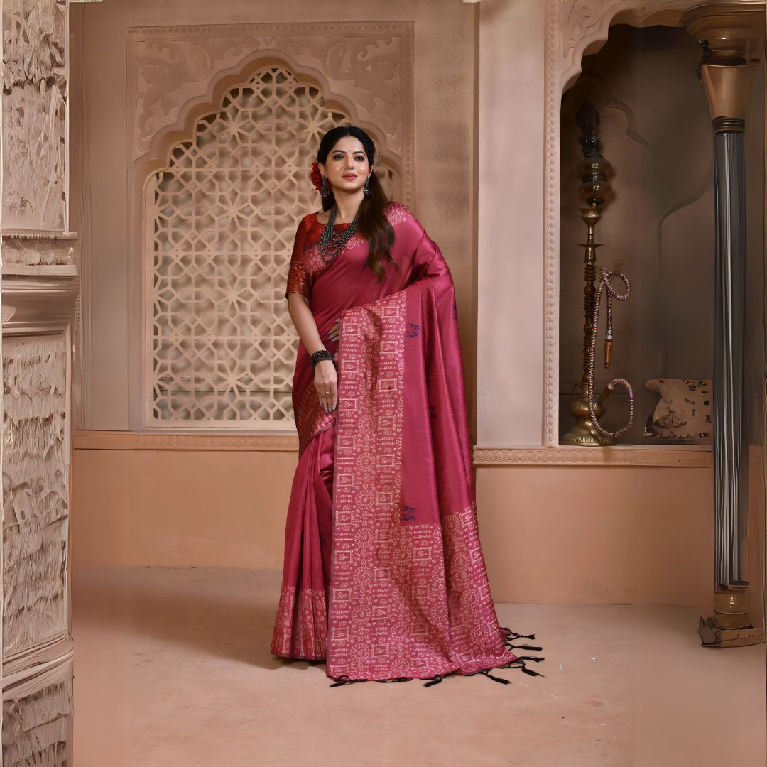 A woman models a striking Dark Pink Banglori Raw Silk Saree. The pallu and border feature dense, traditional Kalamkari-style weaving in a lighter pink/gold Zari. She wears a red blouse and substantial dark gemstone or oxidized silver jewelry, posing in an ornate, traditional setting.