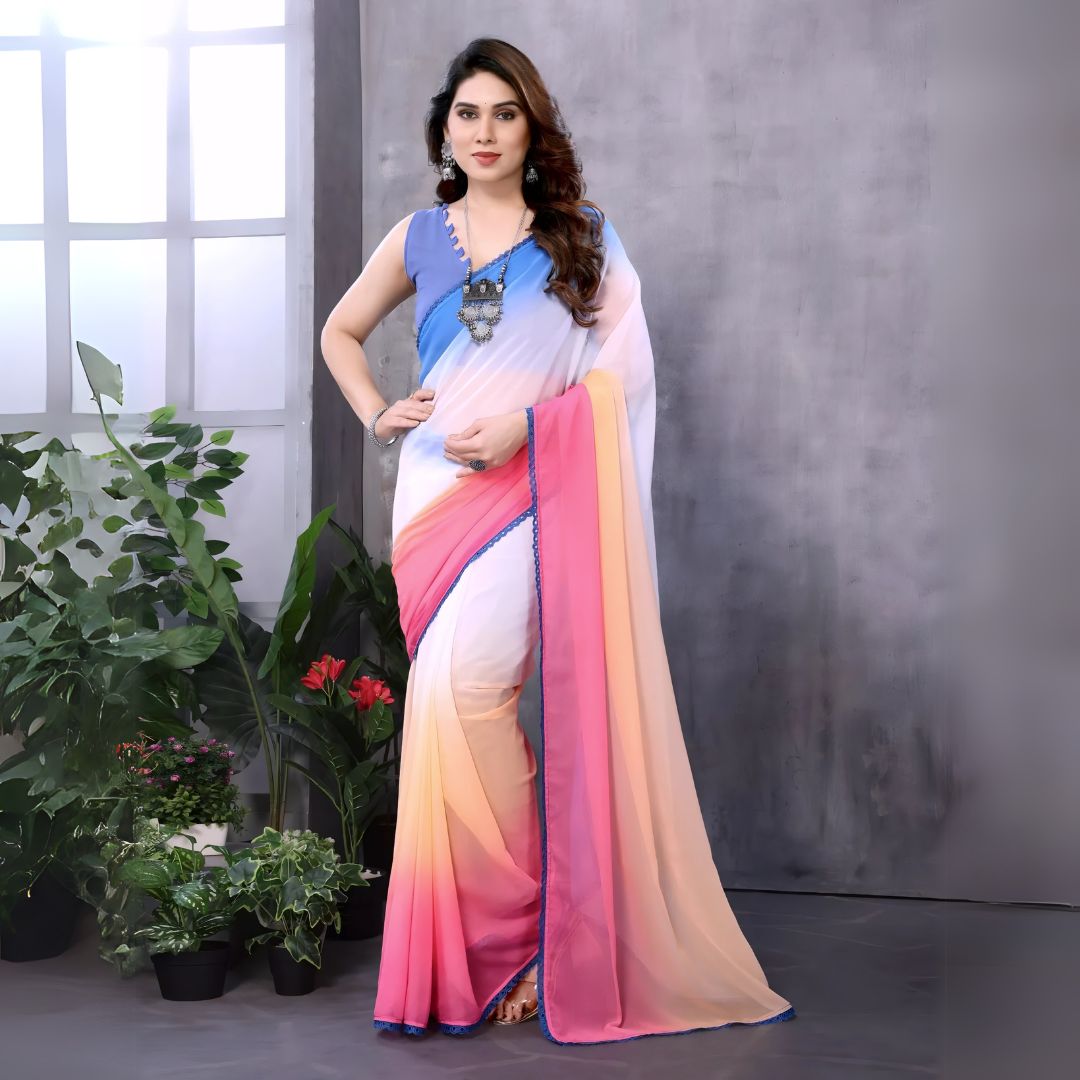 A woman models a vibrant Multicolour Georgette Silk Saree featuring a horizontal ombre color transition from blue at the top to white, pink, and peach at the bottom. The saree has a thin blue border. She pairs it with a light blue sleeveless blouse and a chunky blue and silver necklace.