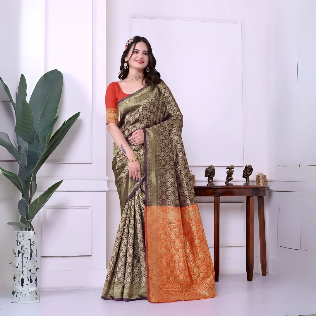 A woman models a striking Dark Brown Banarasi Silk Saree with dense all-over gold Zari weaving. The pallu provides a dramatic contrast in vibrant orange with heavy gold weaving. She wears an orange blouse and gold Kundan jewelry, posing indoors.
