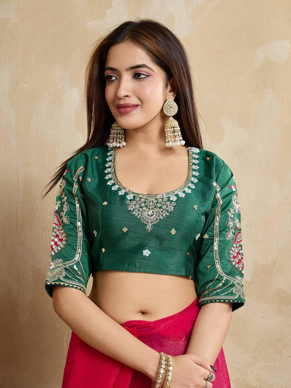A woman models a vibrant Dark Pink Chiffon Silk Saree with scattered embellishments. The saree has a wide, intricate silver embroidery border. She wears a heavily embroidered dark green blouse and accessorizes with silver jewelry, posing indoors.