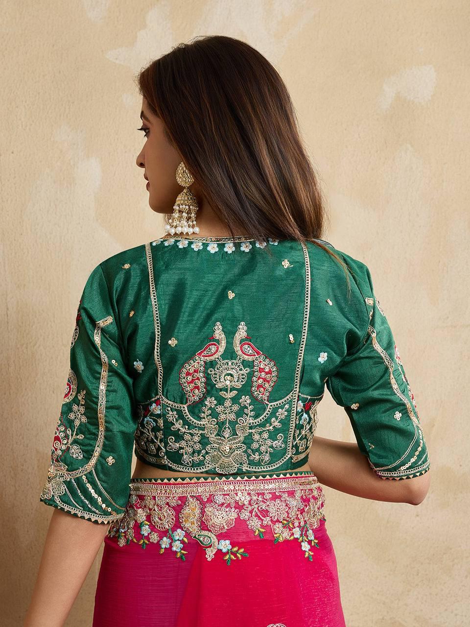 A woman models a vibrant Dark Pink Chiffon Silk Saree with scattered embellishments. The saree has a wide, intricate silver embroidery border. She wears a heavily embroidered dark green blouse and accessorizes with silver jewelry, posing indoors.