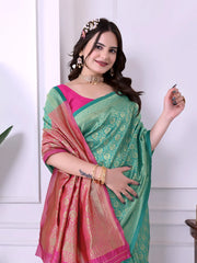A woman models a striking Sea Green Banarasi Silk Saree with dense all-over gold Zari weaving. The pallu and border feature a dramatic contrast with hot pink. She wears a hot pink short-sleeve blouse and gold Kundan jewelry, posing indoors.