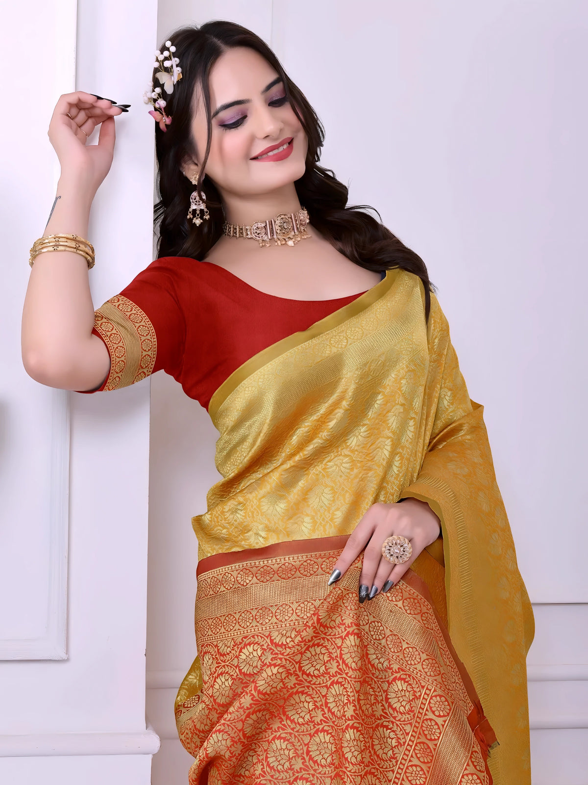 A woman models a striking Golden Yellow Banarasi Silk Saree with dense tone-on-tone Zari weaving. The wide border and pallu feature a dramatic contrast in vibrant red/orange with heavy gold Banarasi weaving. She wears a red blouse and gold Kundan jewelry.