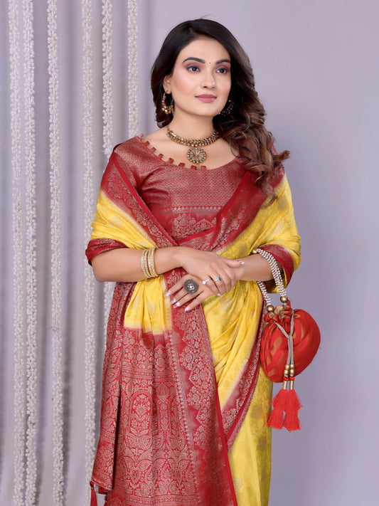Woman wearing a yellow silk saree with a rich maroon embroidered border and matching blouse, styled with traditional jewelry. She poses gracefully in a contemporary studio featuring baskets filled with rose petals and minimal decor, set against a neutral backdrop.